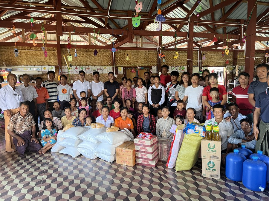 Group photo with families gathered around donated rice, oil, water, and supply boxes