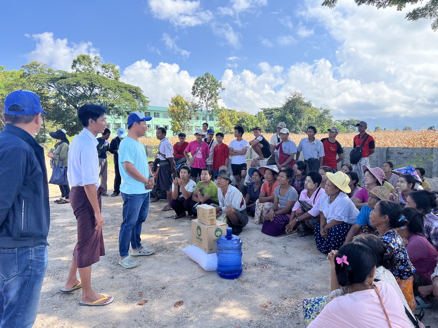 Volunteers meeting with villagers seated outdoors beside relief supplies