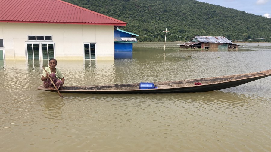 Flooded village scene with a woman traveling by boat past a partially submerged home